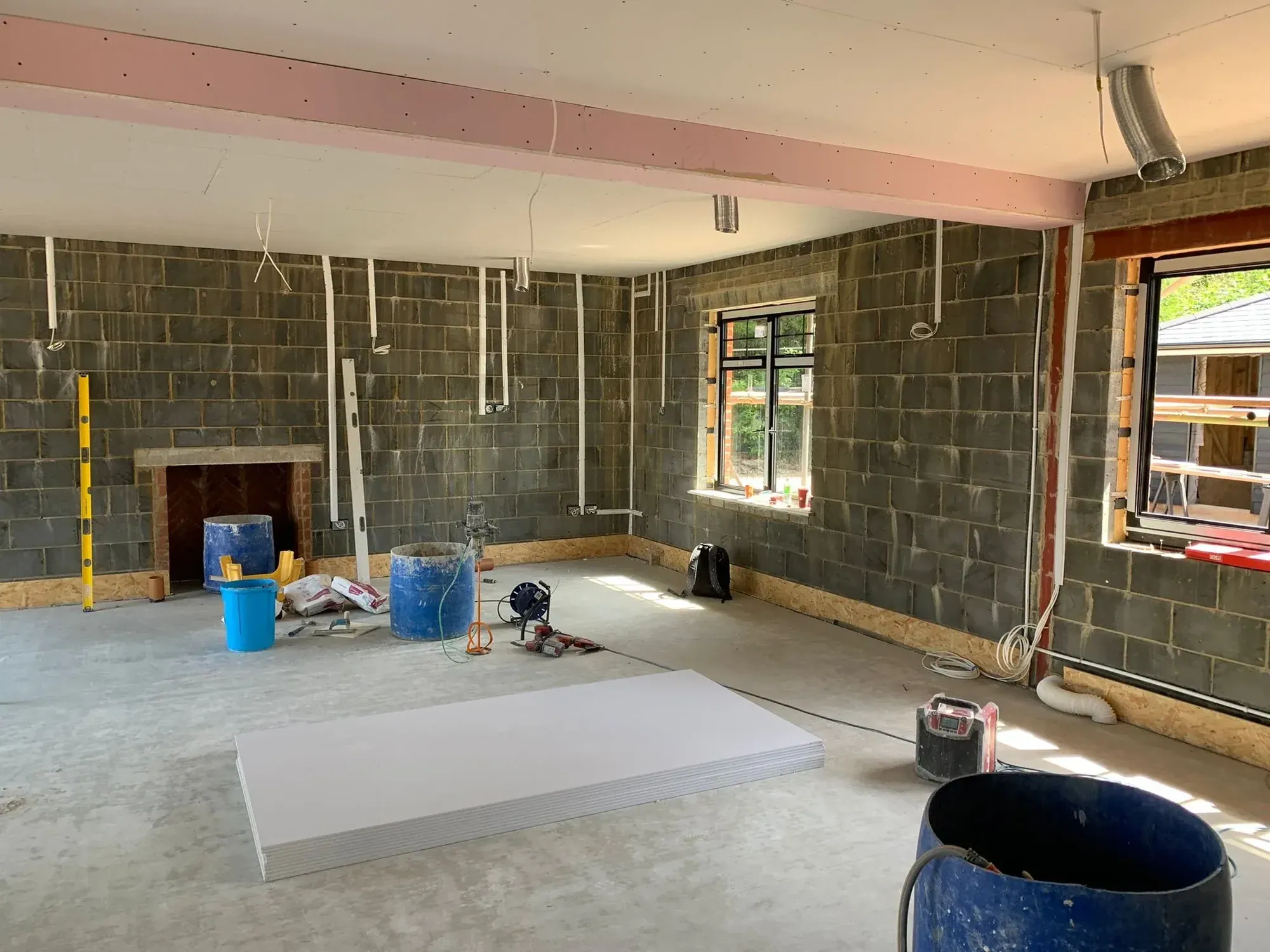 Blockwork shell of a room before lining, first-fix cabling dropped from the ceiling, a rooflight, plasterboard laid on the floor