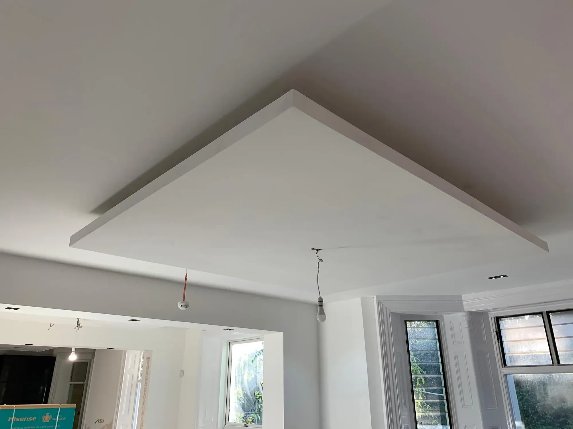 Rectangular plasterboard ceiling raft with a recessed shadow gap above a kitchen, pendant cable hanging, bay window to the right