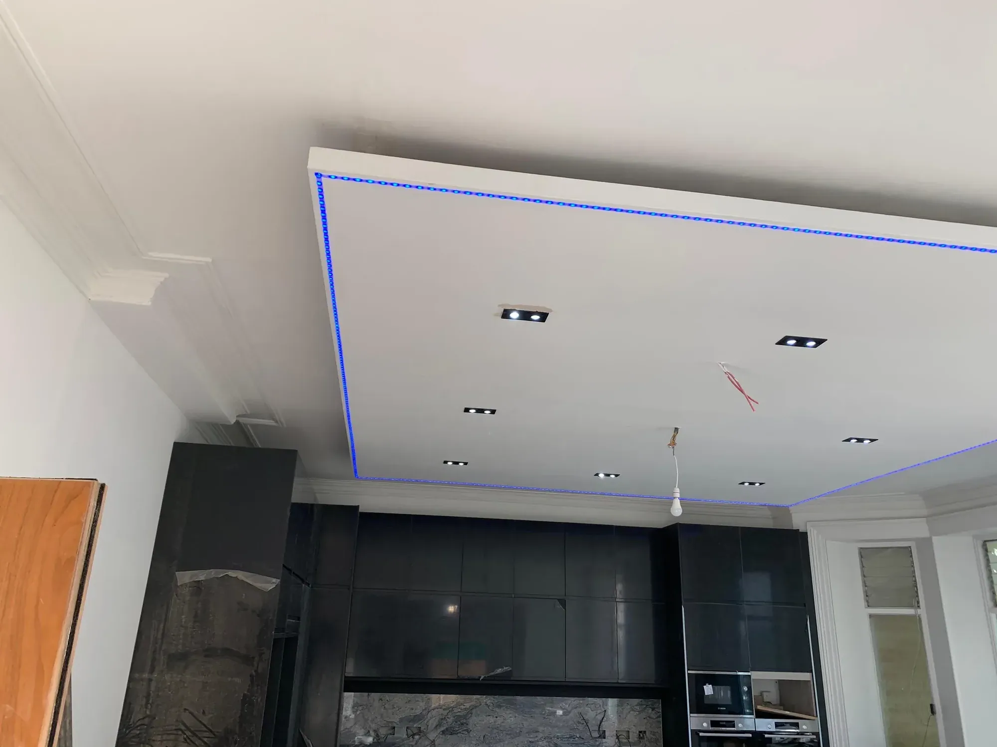 Plasterboard ceiling raft edged with a blue LED strip in its recess, downlights set into the raft, dark kitchen units below