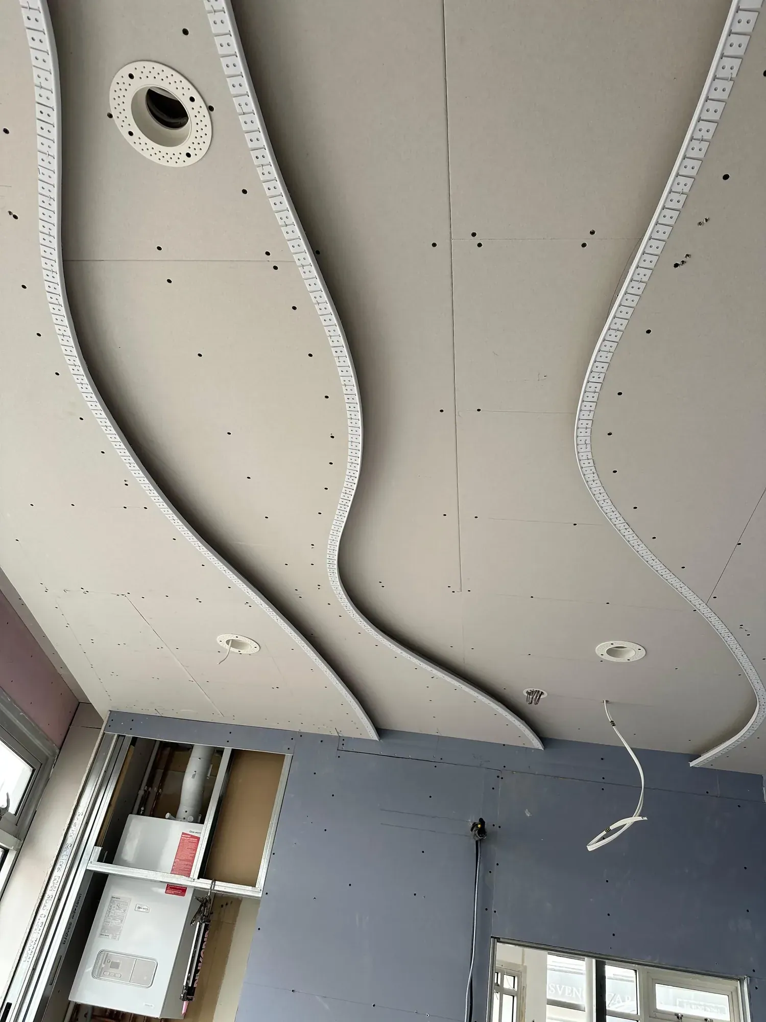 Curved plasterboard bulkhead sweeping across a ceiling, downlight holes cut, walls painted dark blue below