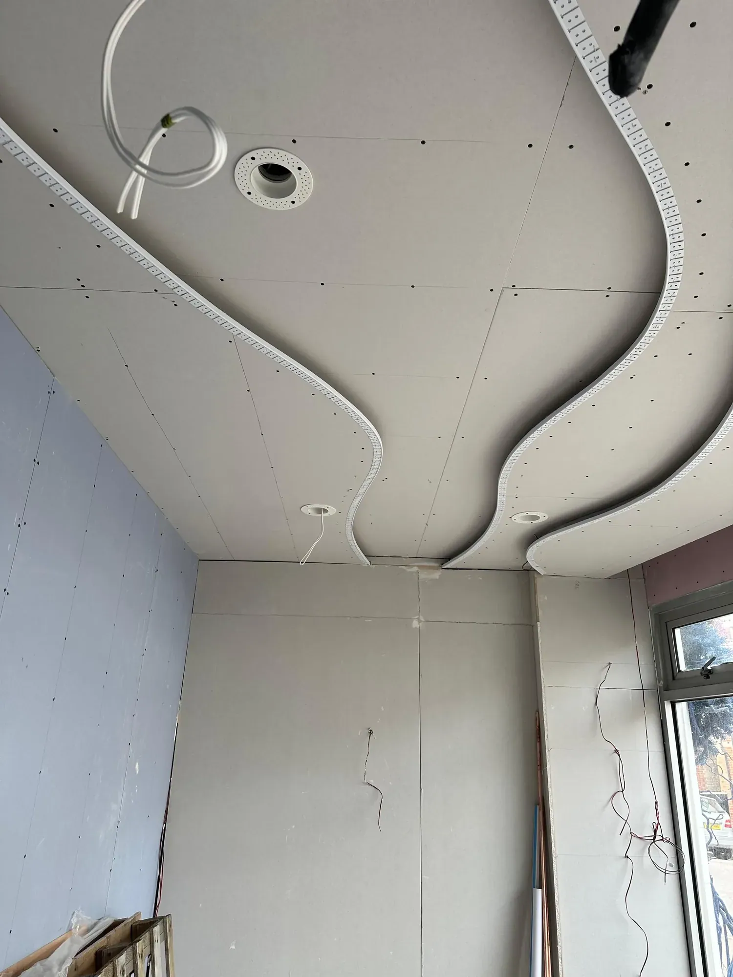 Curved plasterboard ceiling bulkhead with a wave profile, downlight cut-outs, a window to the right