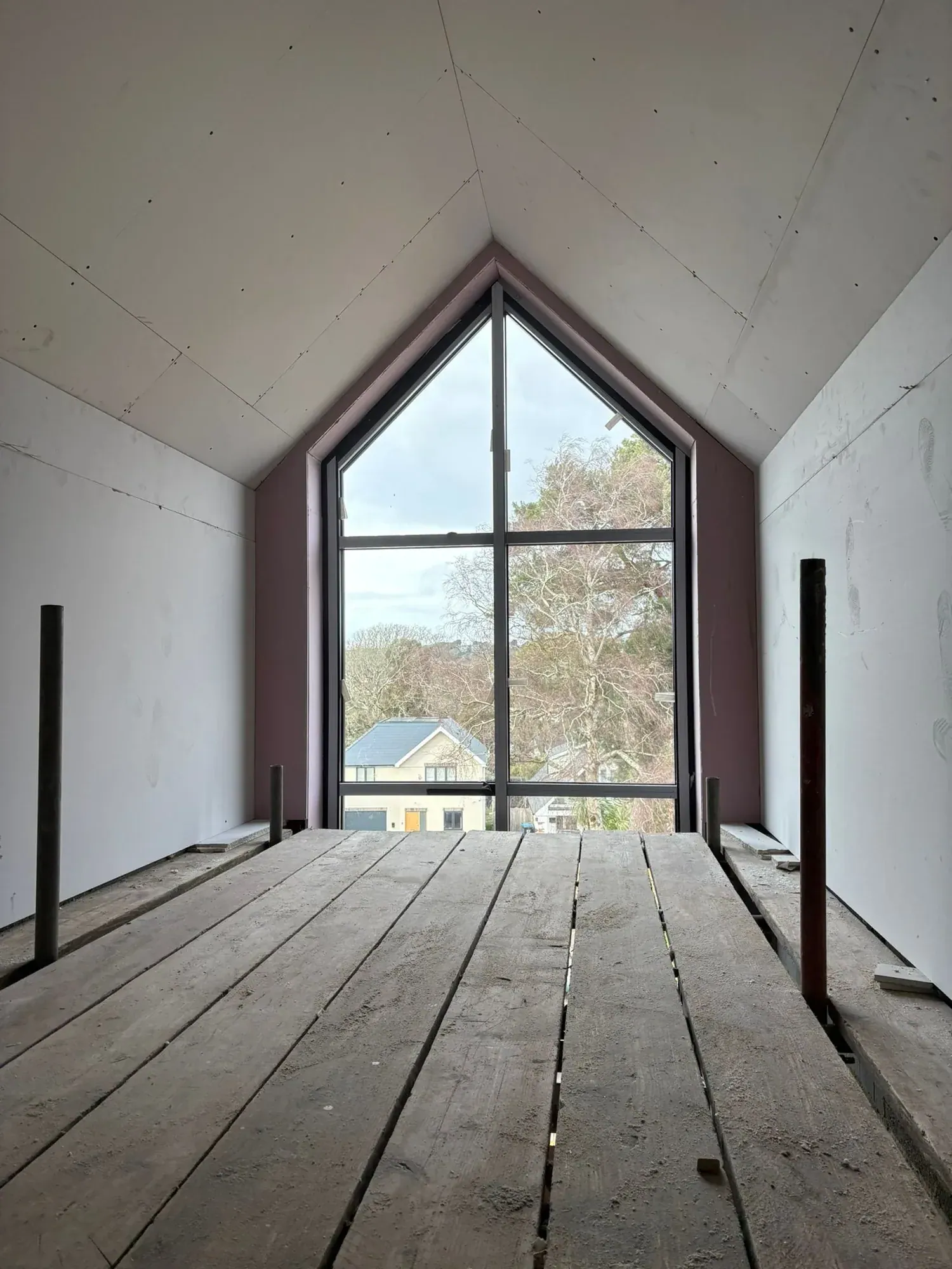 Boarded loft room with a full-height apex window and bare boards on the floor