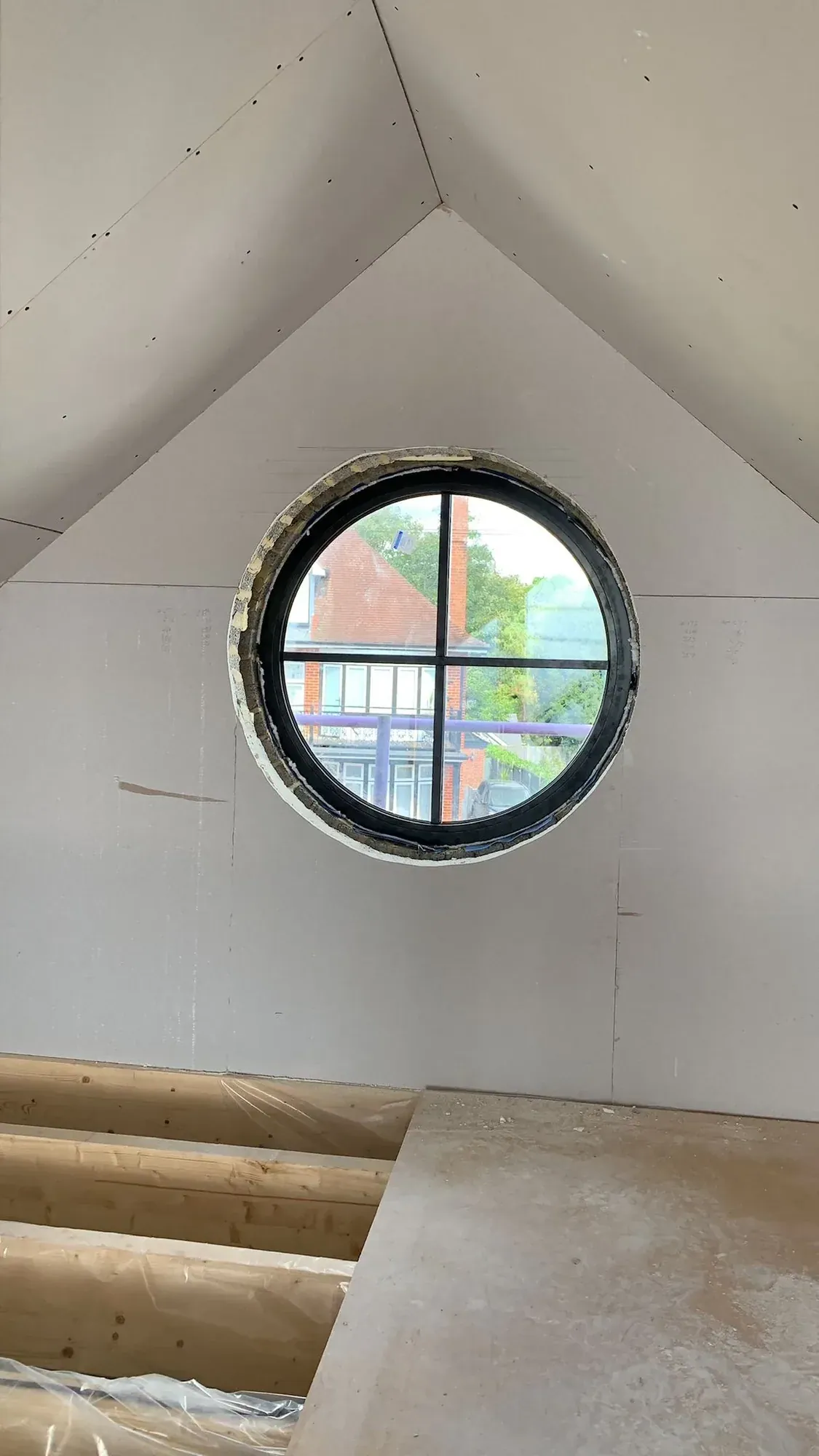Boarded gable wall with a round porthole window and a bare timber floor