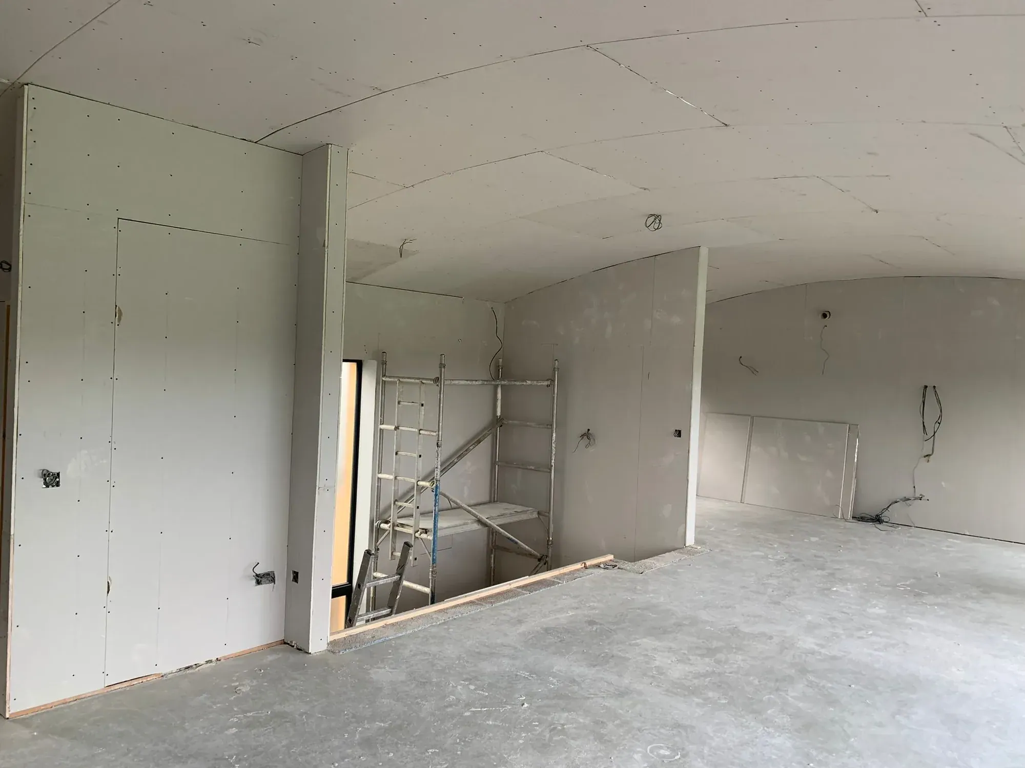 Open-plan room boarded floor to ceiling with a gently curved ceiling, scaffold tower in a doorway