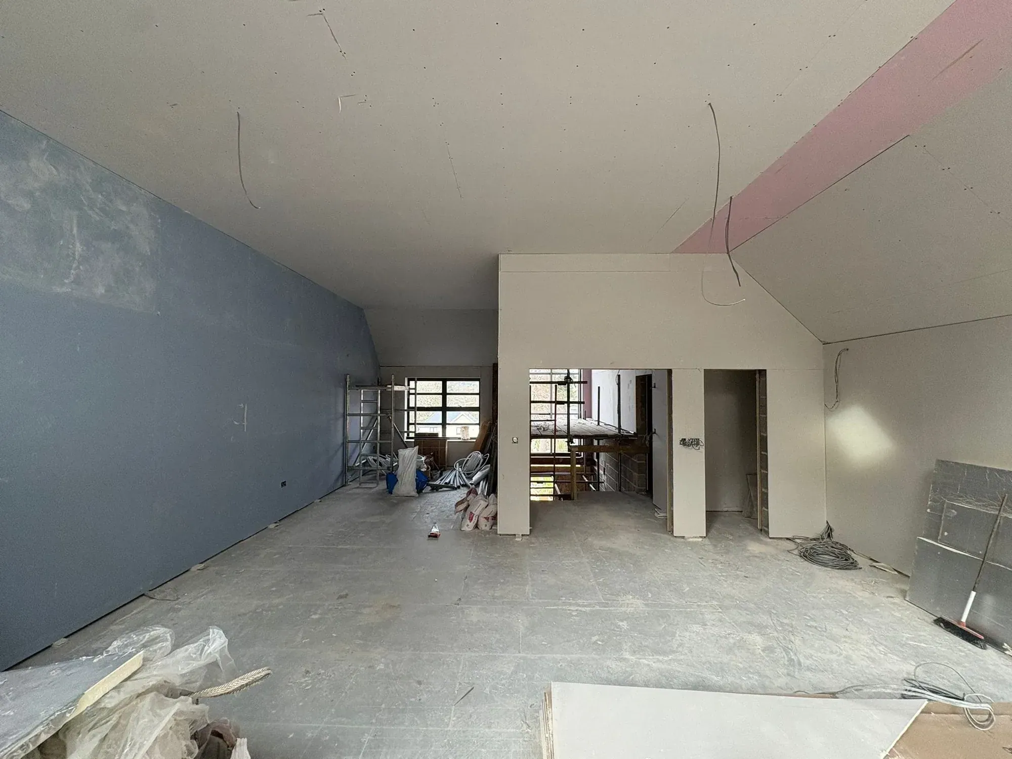 Large open-plan room with a vaulted ceiling fully boarded, pink fire-rated board along the ceiling perimeter, openings framed through to further rooms