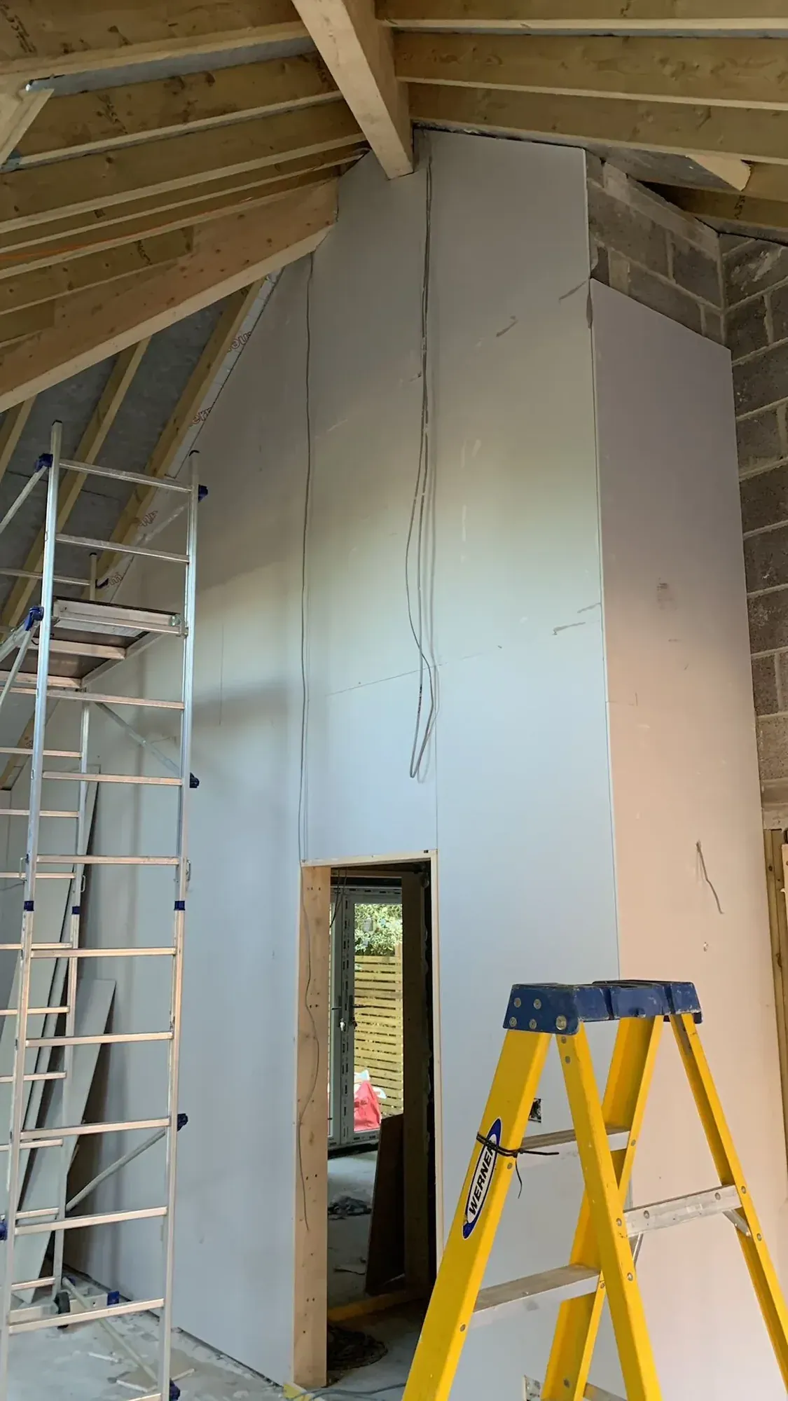 Vaulted ceiling boarded above an exposed blockwork wall, stepladder against the wall