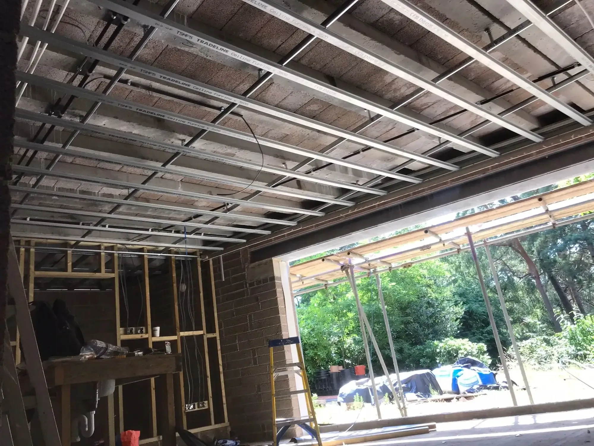 MF ceiling grid installed across a rear extension, open bifold aperture to the garden with scaffold outside