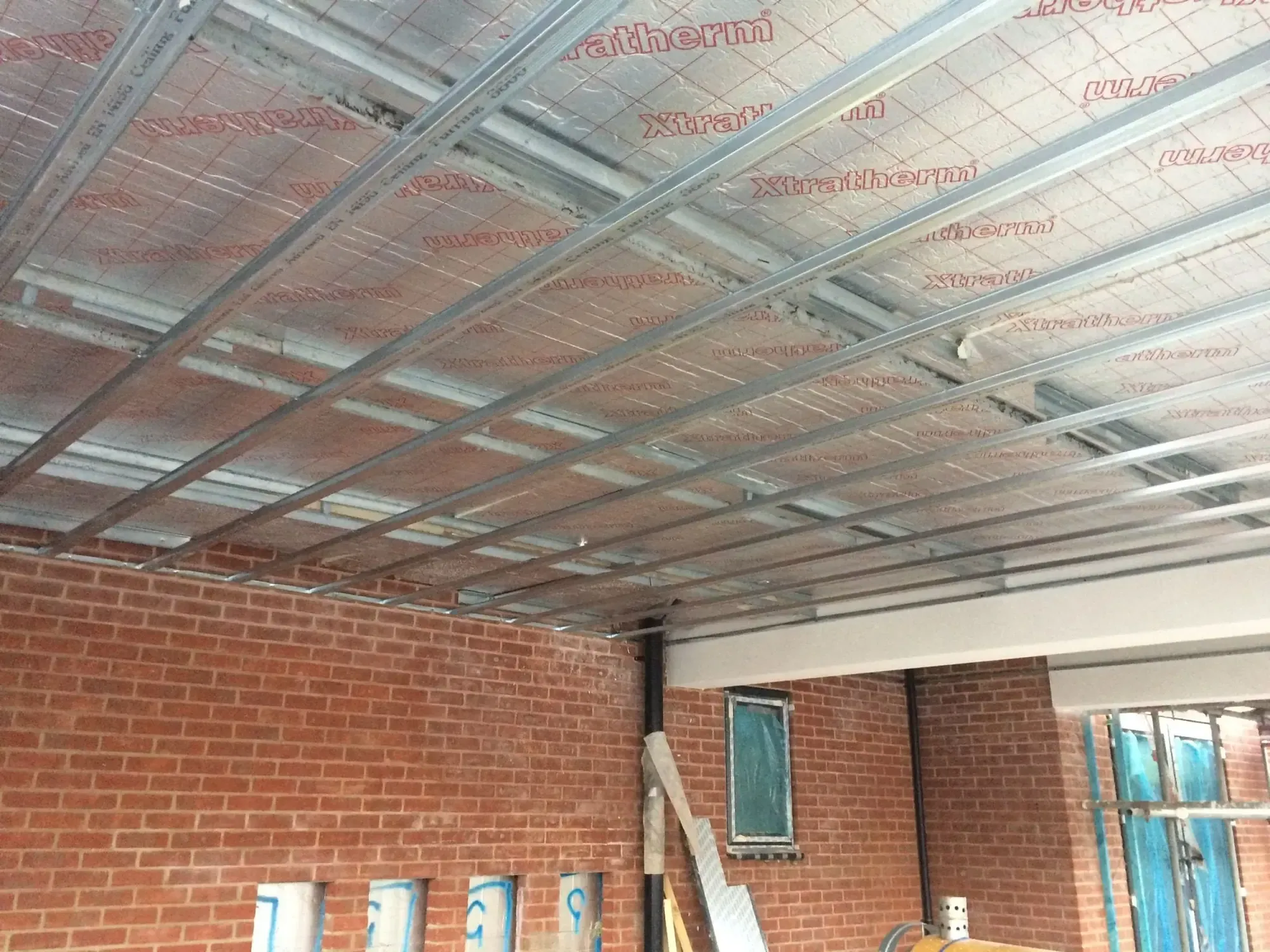 Underside of an MF ceiling grid with insulation quilt above, brick walls below