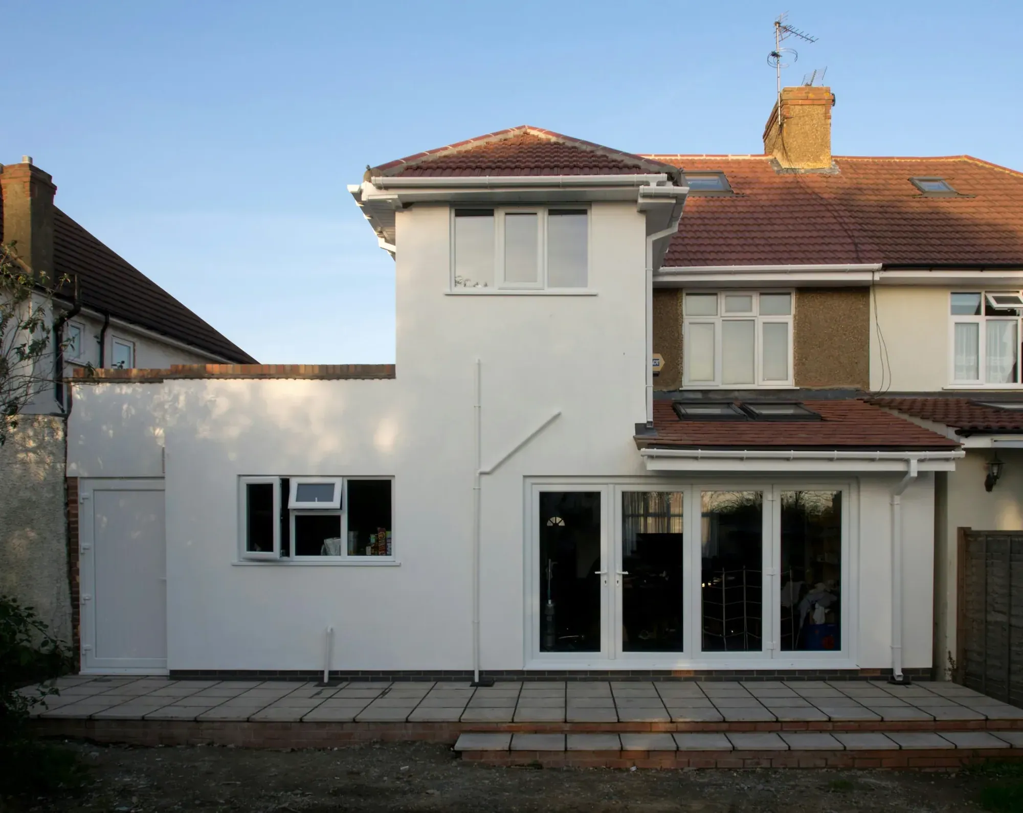 Rear elevation of a semi-detached house freshly rendered and painted white, new patio doors and paving